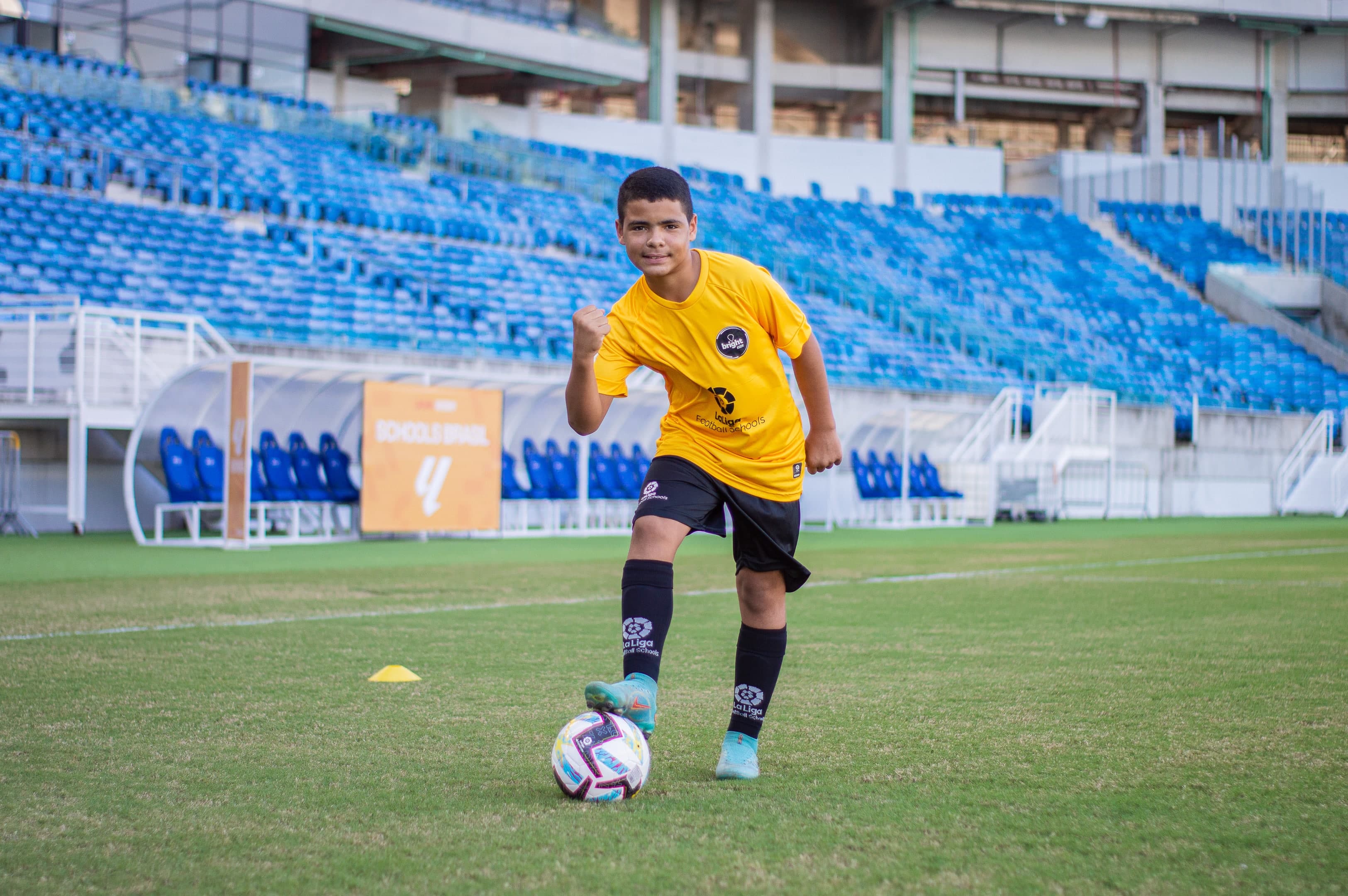 Garoto vestido com uniforme da LALIGA Academy Schools Brasil em estadio de futebol, posando para a foto