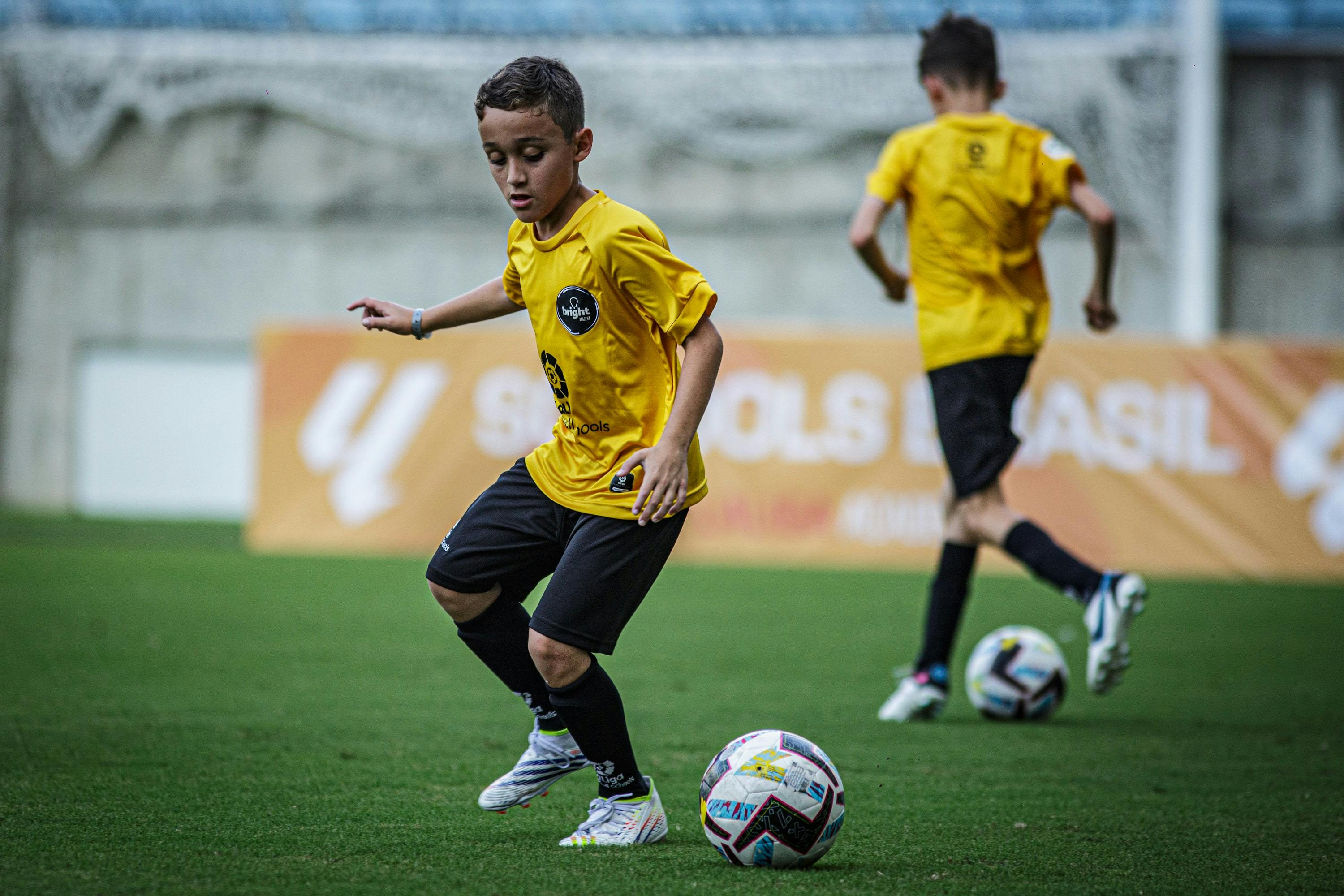 Dois garotos jogando futebol em campo de futebol vestidos com uniforme da LALIGA Academy Schools Brasil