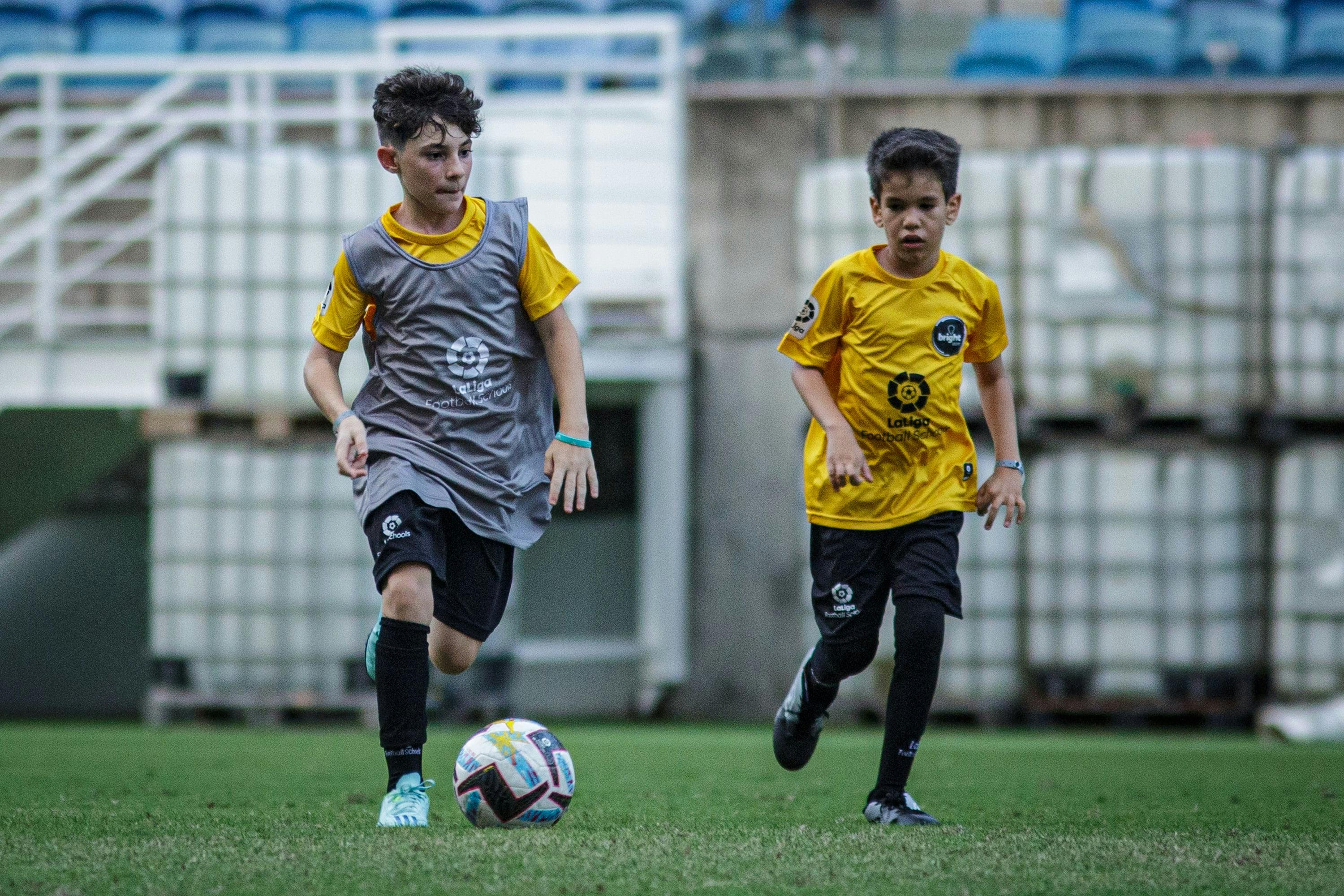 Dois garotos jogando futebol em campo de futebol vestidos com uniforme da LALIGA Academy Schools Brasil
